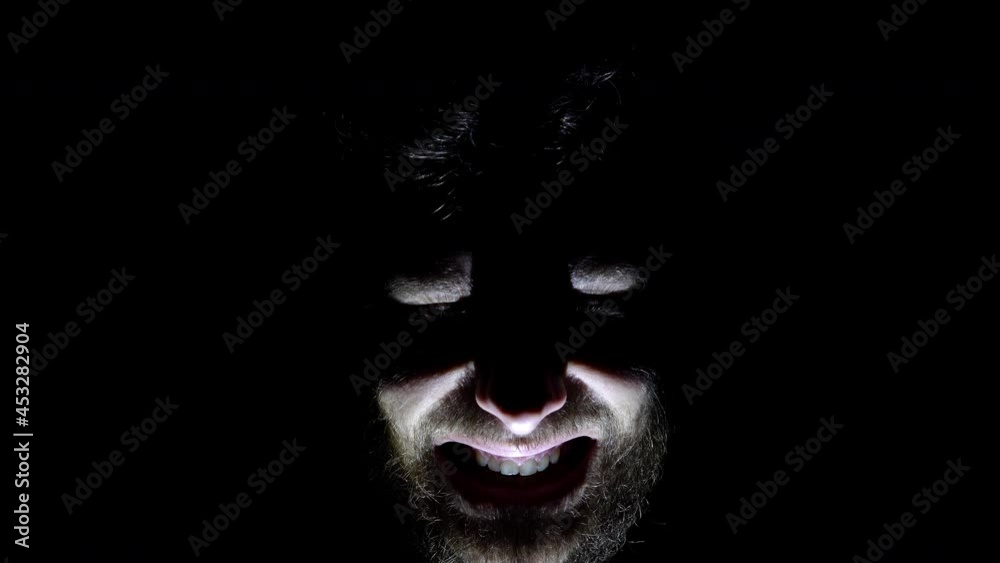 Features of a male overgrown face, backlit in the dark. Close up of a man's face in the dark who laughs Features of a male overgrown face, backlit in the dark. Close up of a man's face in the dark who laughs