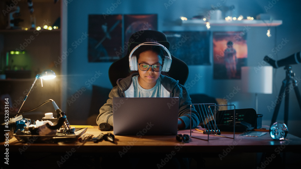 Young Teenage Multiethnic Girl Using Laptop Computer and Putting On Headphones in a Dark Cozy Room at Home. She's Browsing Educational Research Online. Studying Science School Homework Concept. Young Teenage Multiethnic Girl Using Laptop Computer and Putting On Headphones in a Dark Cozy Room at Home. She's Browsing Educational Research Online. Studying Science School Homework Concept.