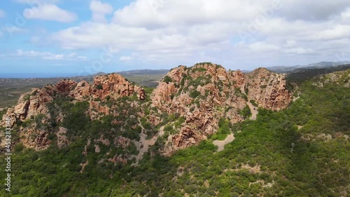 Flying over the top of a rocky mountain with green trees and bushes at the foot