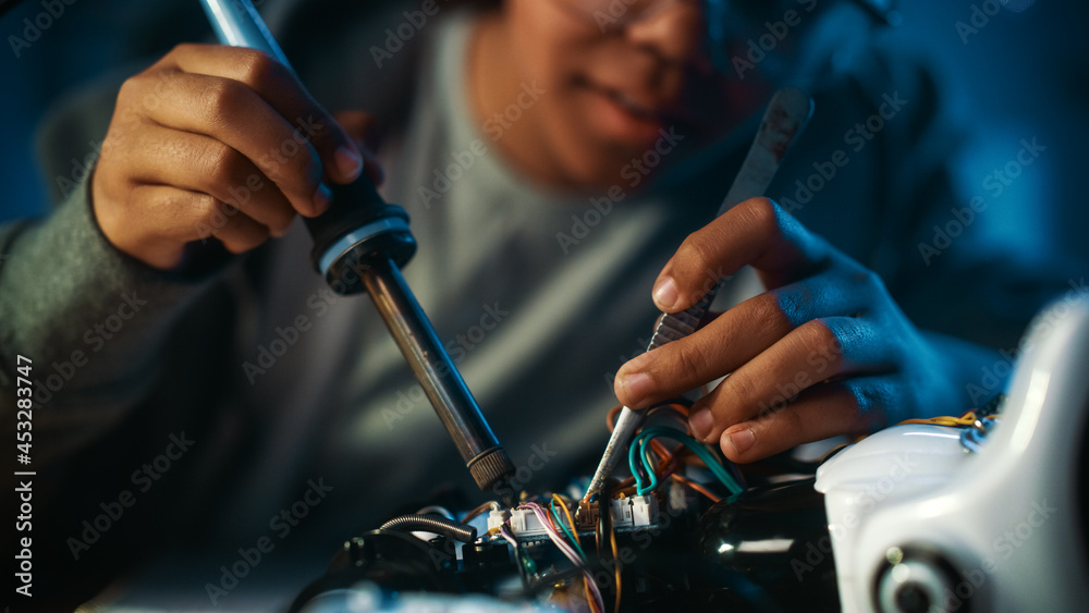 Young Teenage Multiethnic Schoolgirl is Studying Electronics and Soldering Wires and Circuit Boards in Her Science Hobby Robotics Project. Girl is Working on a Robot in Her Room. Education Concept.