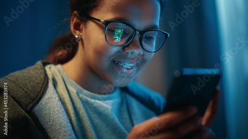 Portrait of a Teenage Multiethnic Black Girl Playing an Arcade Video Game on a Smartphone Application. She Wears Glasses and Dental Braces.