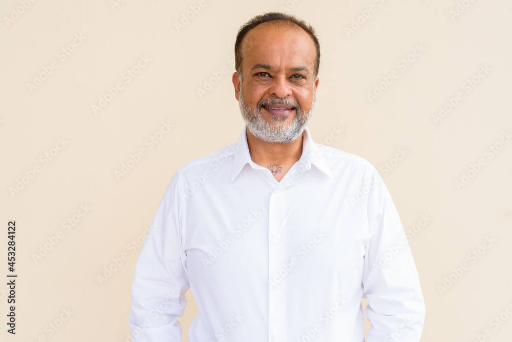 Portrait of happy bearded Indian man smiling against plain wall Portrait of happy bearded Indian man smiling against plain wall