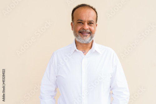 Portrait of happy bearded Indian man smiling against plain wall
