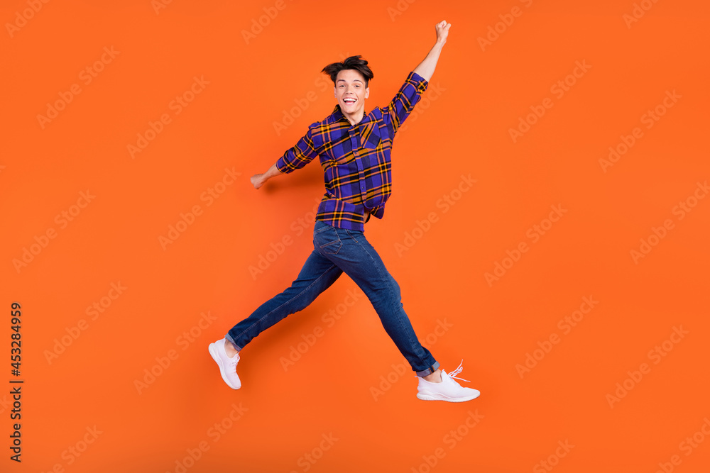 Full body profile photo of millennial funny guy jump wear shirt jeans sneakers isolated on orange background