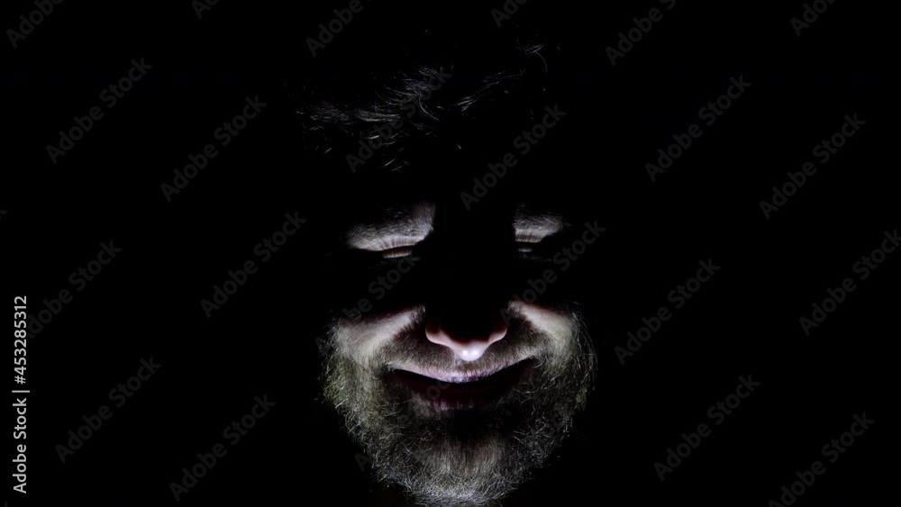Features of a male, bearded face, backlit in the dark. Close up of a man's face in the dark who smiles
