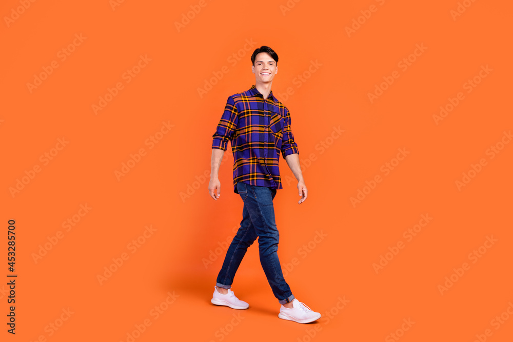 Photo of pretty sweet teenager man dressed checkered clothes walking smiling isolated orange color background Photo of pretty sweet teenager man dressed checkered clothes walking smiling isolated orange color background