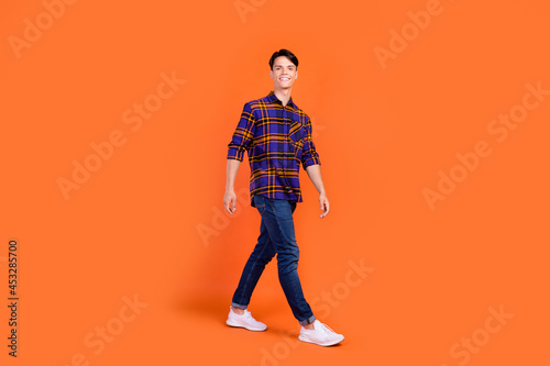 Photo of pretty sweet teenager man dressed checkered clothes walking smiling isolated orange color background