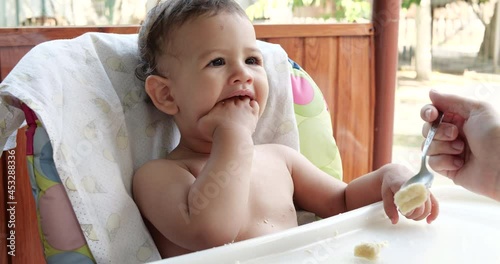portrait of a child who eats baby food with his spoon. mother feeds the child on the outdoorat the children's table