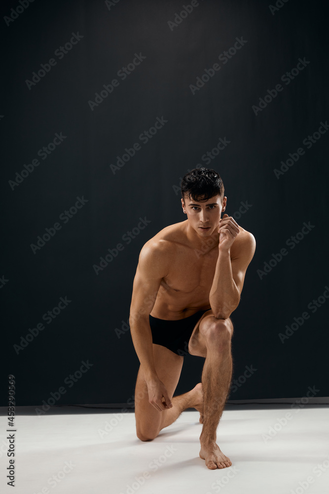 sporty man in black shorts kneels on a dark background