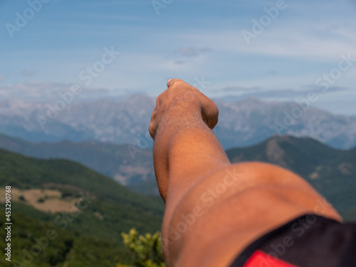 Close-up of woman's arm pointing to the mountains that are the Picos de Europa in Spain, on a sunny summer day