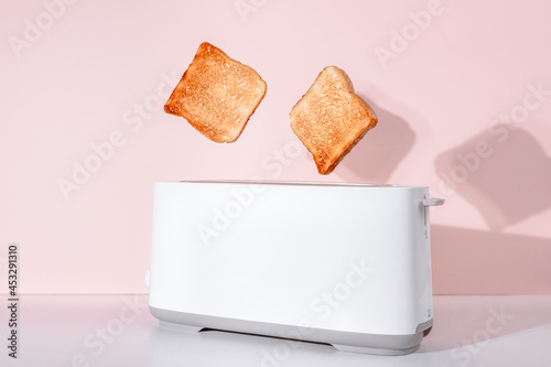 Toasts jumping out of white toaster. Levitation food. Delicious breakfast concept. Pink background. Flat lay, side view. Kitchen equipment for fresh morning meal. Toasted bread for sandwich.