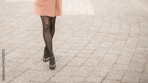 No face close up on legs making a cat walk of young woman on the street wearing autumn black shoes. Stylish young woman wearing autumn coat black nylon tights outdoors. Autumn accessories. 