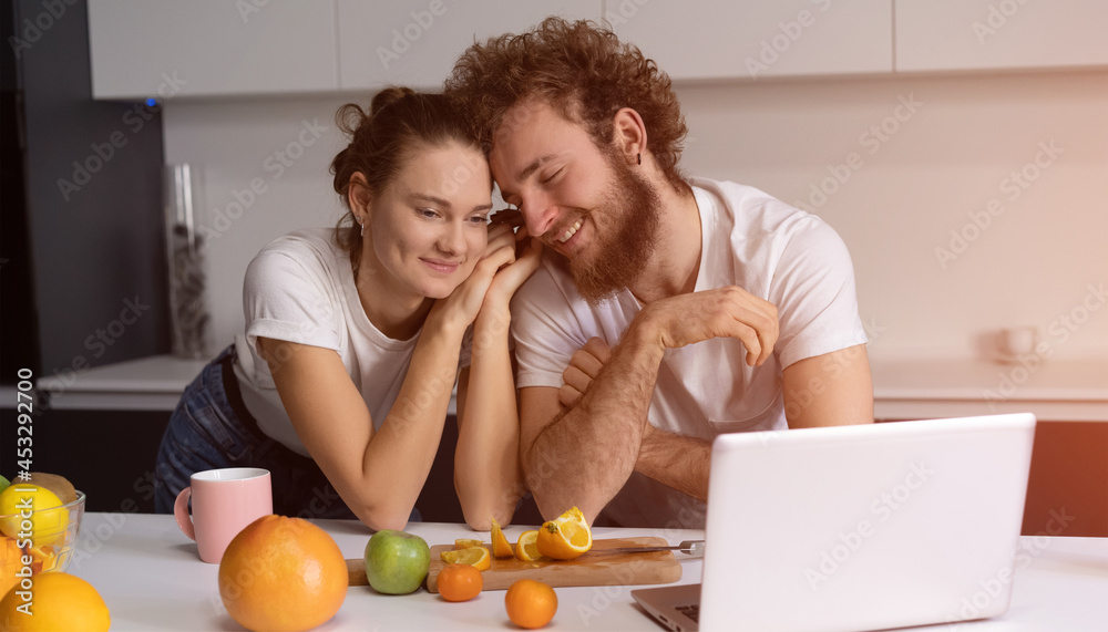 Beautiful young couple talking on video call using laptop. Young couple cooking healthy food in kitchen at home. Man leaned on girl smiling watching romantic movie. Beautiful young couple talking on video call using laptop. Young couple cooking healthy food in kitchen at home. Man leaned on girl smiling watching romantic movie.