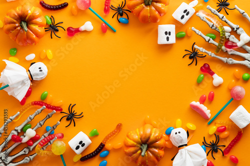 Halloween background. Frame of jelly beans  warms  ghost marshmallows  pumpkins  spiders on orange background. Flat lay  top view  overhead.