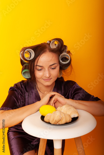 a girl in curlers looks at croissans a housewife cooked homemade cakes on a yellow isolated background photo