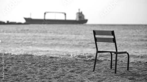 Lonely beach with empty chair and a vessel in the sea on the background. chair on sandy beach at sunset - relaxation concept