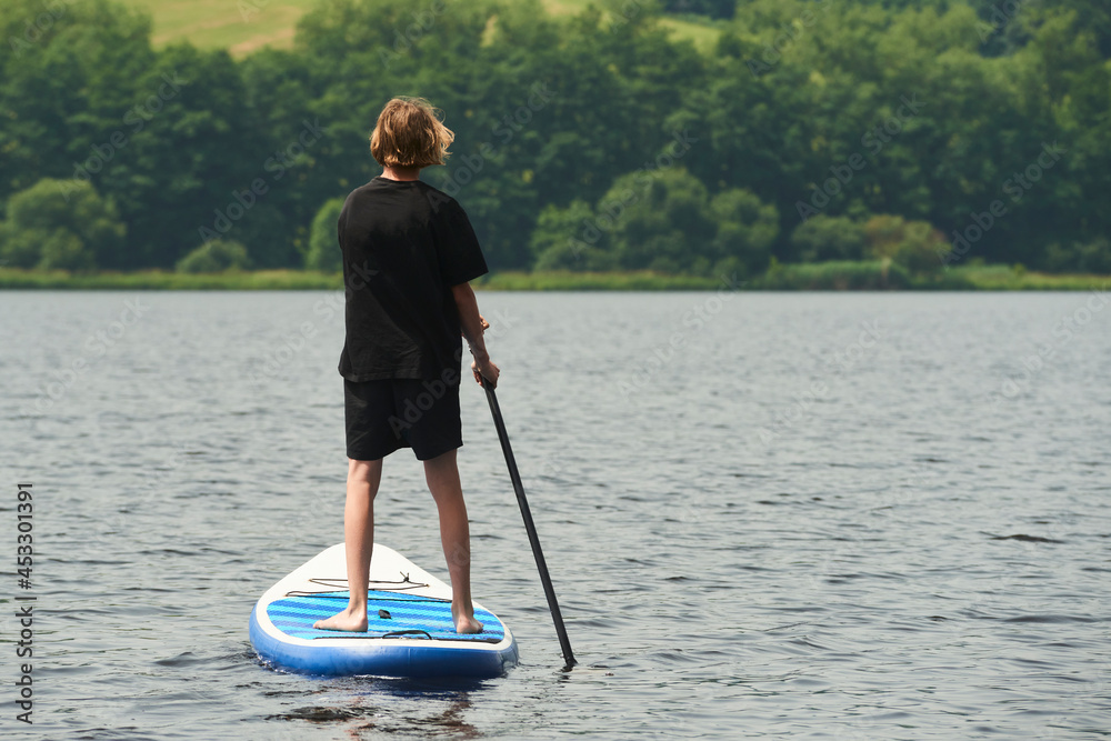 Boy rowing on stand up paddle boarding (SUP) paddling along the calm lake. The concept of children's sports and tourism.
Boy rowing on stand up paddle boarding (SUP) paddling along the calm lake. The concept of children's sports and tourism.