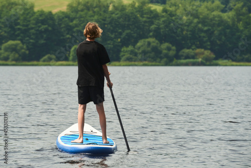 Boy rowing on stand up paddle boarding (SUP) paddling along the calm lake. The concept of children's sports and tourism. 