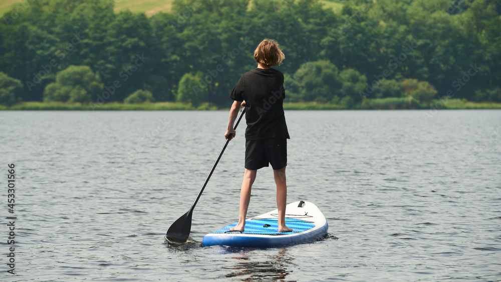 Boy rowing on stand up paddle boarding (SUP) paddling along the calm lake. The concept of children's sports and tourism.
Boy rowing on stand up paddle boarding (SUP) paddling along the calm lake. The concept of children's sports and tourism.