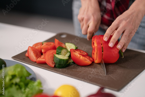 Cuts vegetables for a fresh salad young housewife cut bell pepper, cucumber, tomato on cutting board preparing for a family dinner standing in the new kitchen of a new home. Healthy lifestyle. 