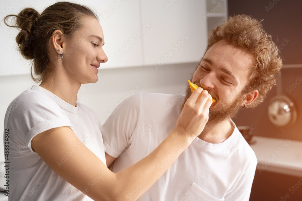Pretty girl feeds or nursing her boyfriend. Beautiful young couple feeding each other, making fun at modern kitchen and smiling while cooking at home. Pretty girl feeds or nursing her boyfriend. Beautiful young couple feeding each other, making fun at modern kitchen and smiling while cooking at home.