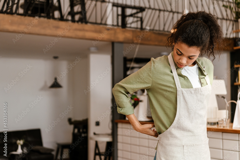 Young black waitress wearing apron while getting ready for work in cafe Young black waitress wearing apron while getting ready for work in cafe