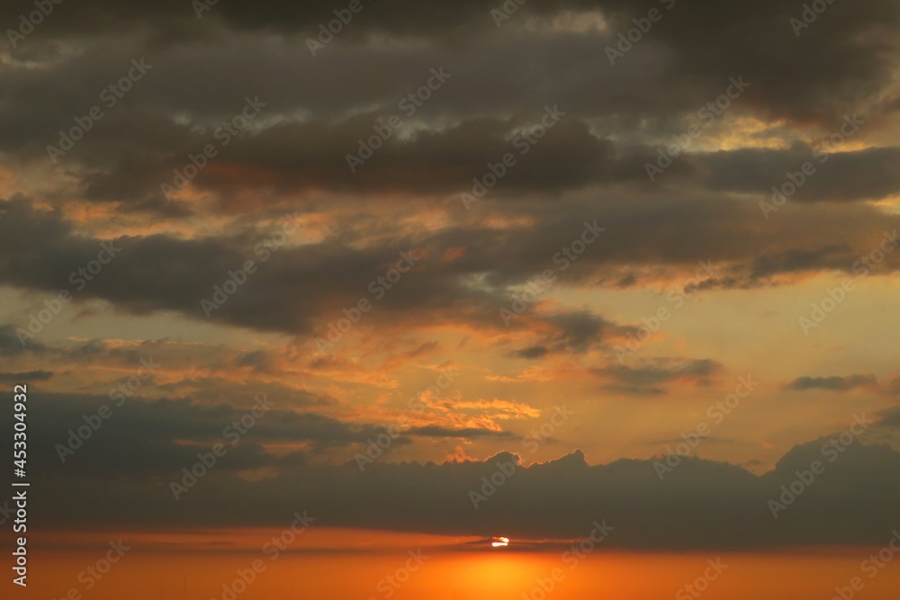 Orange dark dramatic sunset with black clouds in the sky, natural sunset background 