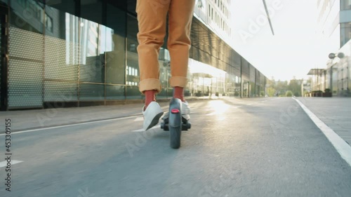 Low section following shot of legs of unrecognizable man riding electric scooter on urban road photo