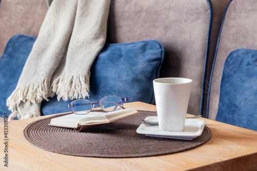 On a wooden table there is a tall coffee cup with coffee, a book with women's glasses.  photo