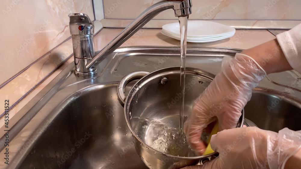 washing silver pan in kitchen sink.  Close up of faucet female hand in gloves