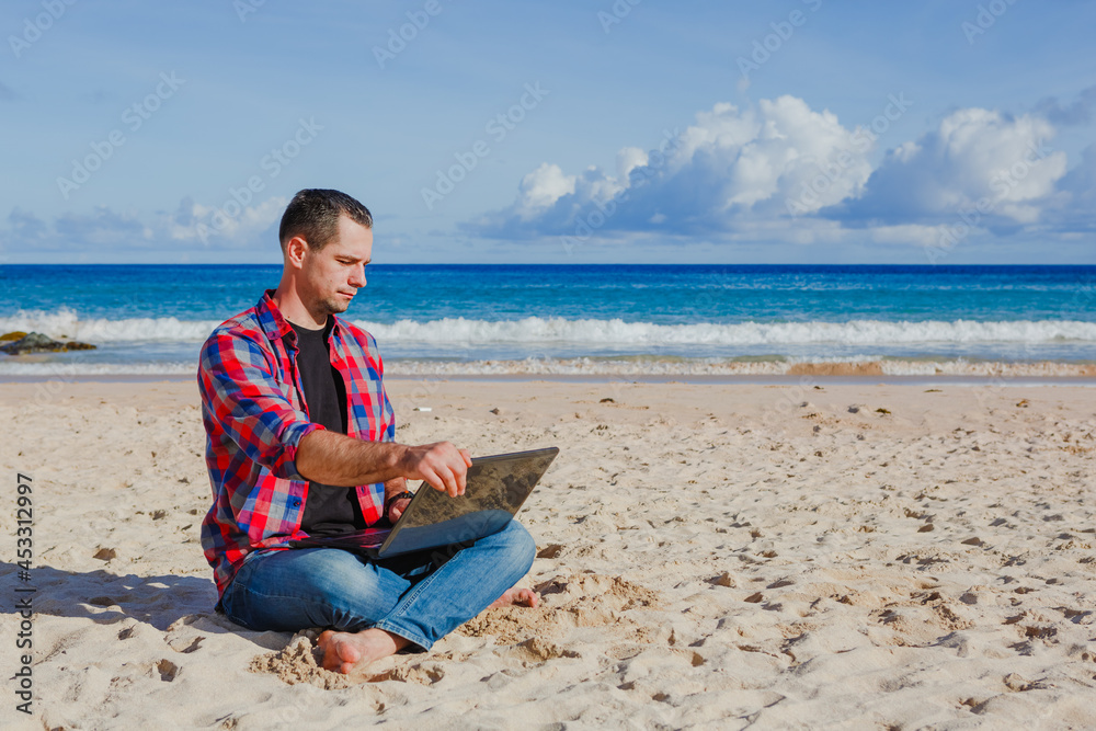 Young man with laptop working on the sand beach