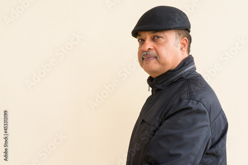 Portrait of handsome Indian man with mustache wearing hat against plain wall