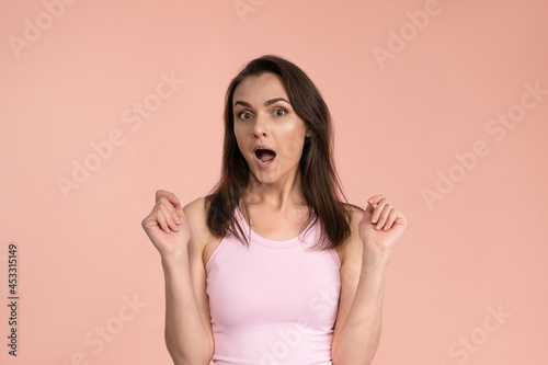 Acting young woman expressing OMG wearing pink t-shirt with hands on her face, excited and joy expression on her face with positive emotions. Facial expressions, emotions, feelings.