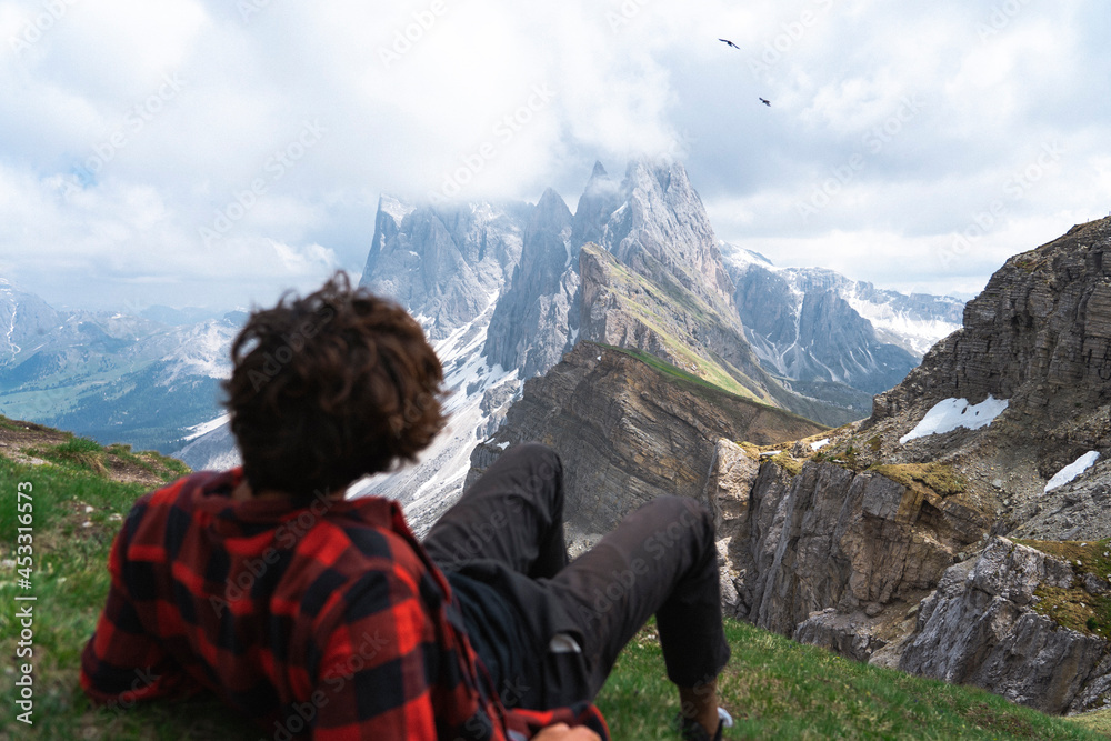 Young hiker in plaid shirt on cloudy, Seceda mountain peak. Traveling to Puez Odle, Dolomites, Trentino, Italy.