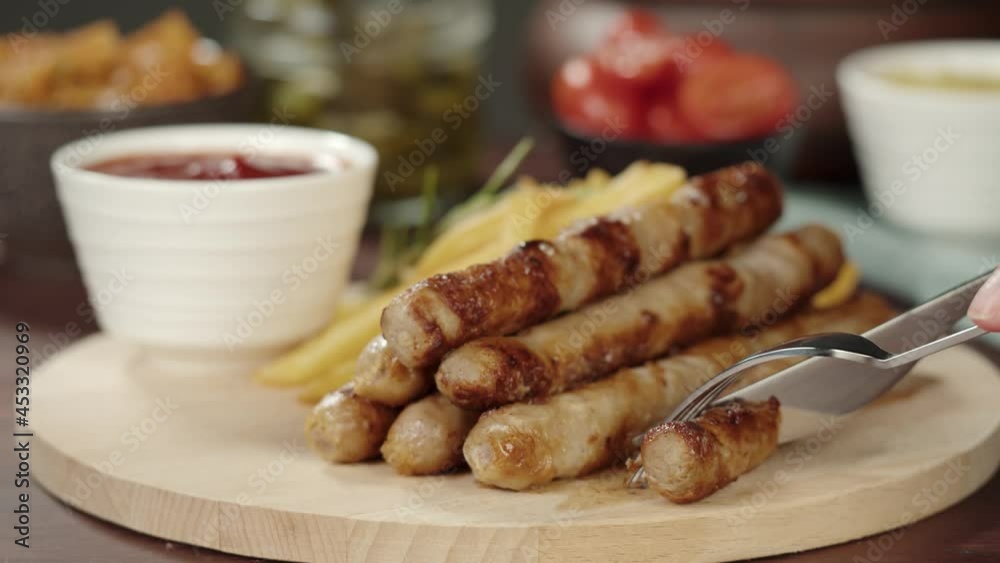 Taking smoked sausages with fork and cutting, fried potatoes and sauce close-up. Traditional German cuisine, bratwursts and potatoes on the table. Composition of cooked national Czech Food. Taking smoked sausages with fork and cutting, fried potatoes and sauce close-up. Traditional German cuisine, bratwursts and potatoes on the table. Composition of cooked national Czech Food.