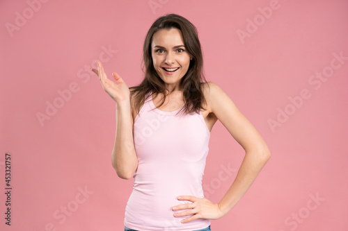Have an idea young caucasian woman with dark hair in pink t-shirt looking at camera with suspicious expression  holding hand on her waist. Facial expressions  emotions  feelings.