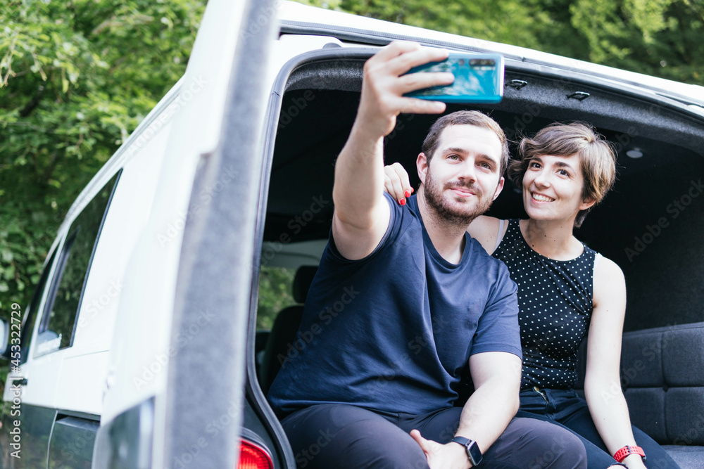 Young happy couple taking selfie in front of their yellow self-converted off-grid camper van