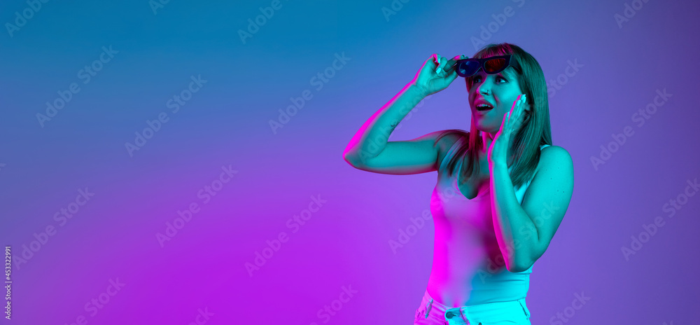 Portrait of young beautiful girl isolated on blue studio background in neon light filter. Concept of human emotions, facial expression, youth, sales, ad. Portrait of young beautiful girl isolated on blue studio background in neon light filter. Concept of human emotions, facial expression, youth, sales, ad.