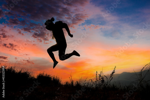 Silhouettes of men jumping with joy and freedom In the meadow during the evening time. man jump high and step on the sun in the silhouette.