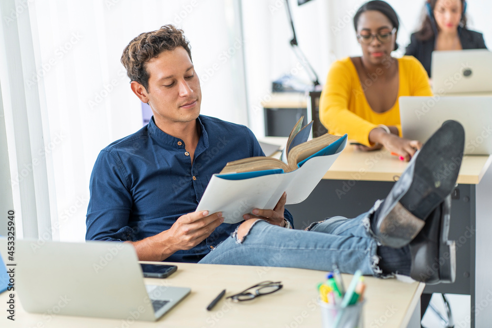 handsome male employee sits and thinks about the work, looks at the documents, works happily while resting, thinking, and putting his feet on the desk at the company. handsome male employee sits and thinks about the work, looks at the documents, works happily while resting, thinking, and putting his feet on the desk at the company.