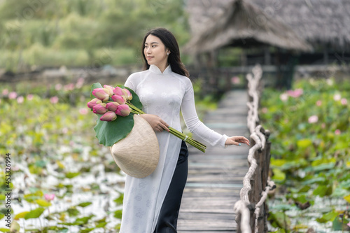 Portrait of beautiful vietnamese woman with traditional vietnam hat holding the pink lotus walking on the wooden bridge in big lotus lake, vietnam, aisan or southeast asia travel concept