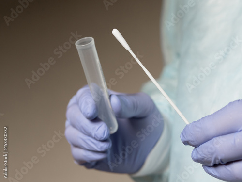Hands in medical gloves holding an oral sample swab and a test tube for covid test