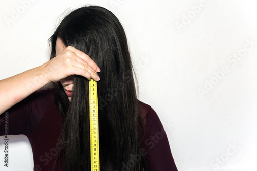 Mujer morena sosteniendo una cinta métrica amarilla para medir la longitud de su cabello largo y negro photo