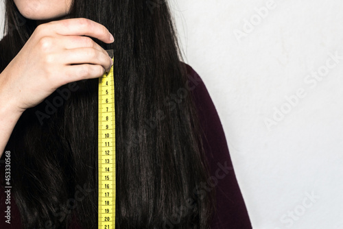 Detalle de una mujer morena sosteniendo una cinta métrica amarilla para medir la longitud de su cabello largo y negro photo