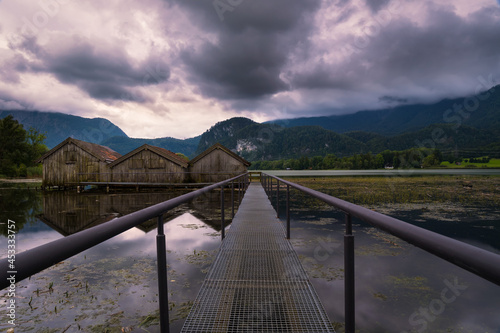 Obraz na plátne View on boat houses at lake Kochelsee on cloudy summer day, vanishing point pers