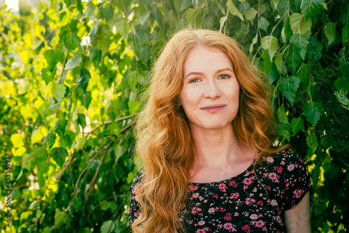 Close-up portrait of lovely lady with long red ginger hair and freckles smiling looking at camera in park in summer. People in nature and happiness concept