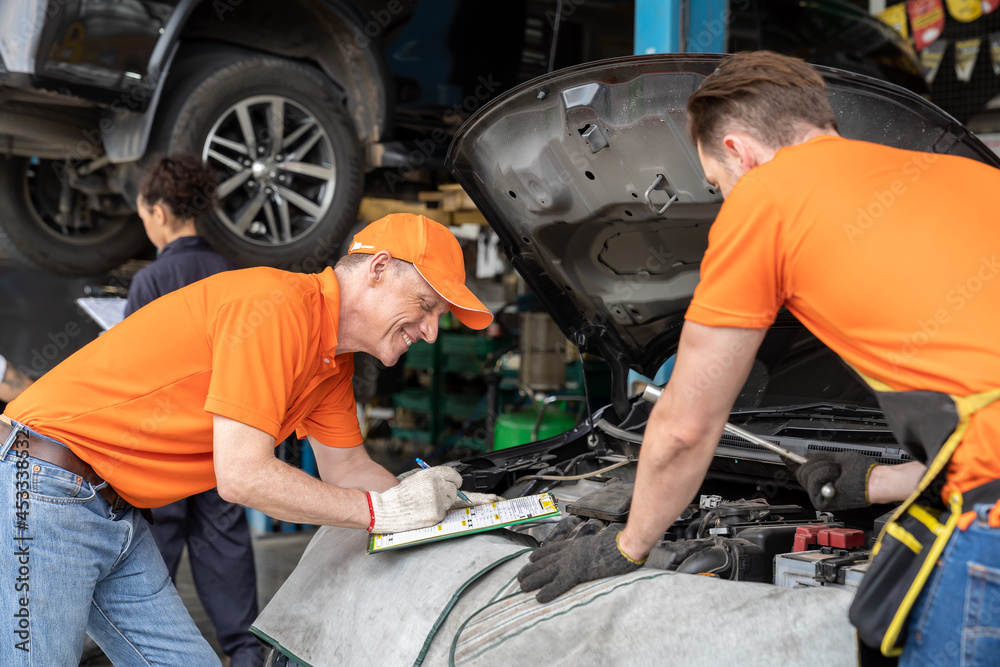 Team of mechanic worker working at the garage. Group of professional mechanic examining, repair and maintenance under hood of car at auto car repair service. Car service and Maintenance concept Team of mechanic worker working at the garage. Group of professional mechanic examining, repair and maintenance under hood of car at auto car repair service. Car service and Maintenance concept
