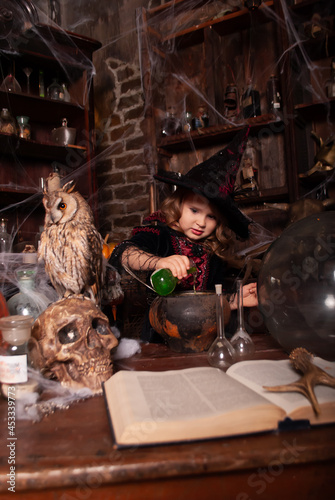 girl charming little witch conjuring potions for Halloween with an assistant oy oy on the table with a place for text