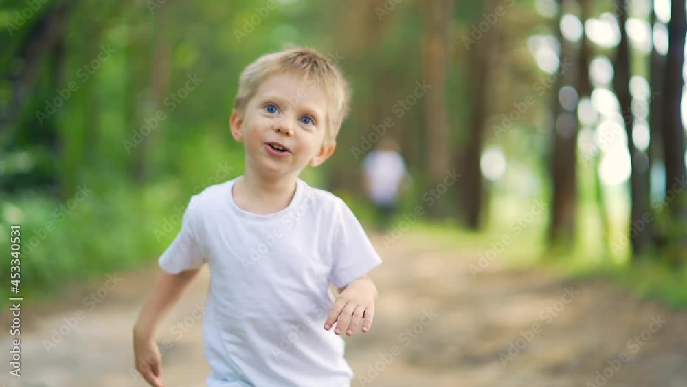 Close up portrait young happy cheerful kid. child running through woods. little boy having fun run. look camera on alley park forest. Happiness preschool blond blue eyes smiling toddler coming forward Close up portrait young happy cheerful kid. child running through woods. little boy having fun run. look camera on alley park forest. Happiness preschool blond blue eyes smiling toddler coming forward