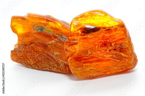 Two pieces of Baltic amber on a white background. Polished transparent sun stone. Natural semi-precious mineral. Material for jewelers. Multicolored yellow-red background. Copal. Macro shooting. 